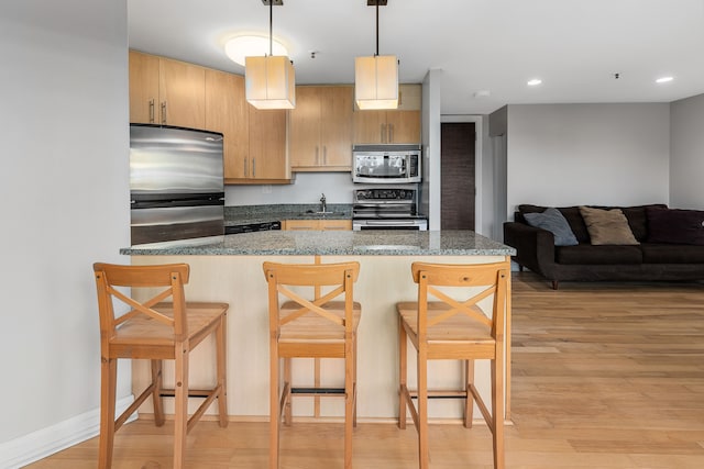 kitchen featuring light hardwood / wood-style flooring, stone countertops, decorative light fixtures, a breakfast bar area, and appliances with stainless steel finishes