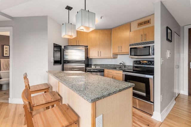 kitchen featuring stainless steel appliances, sink, decorative light fixtures, stone counters, and light hardwood / wood-style floors