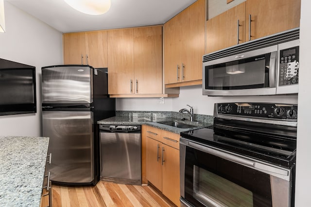 kitchen with stone counters, light wood-type flooring, sink, and appliances with stainless steel finishes