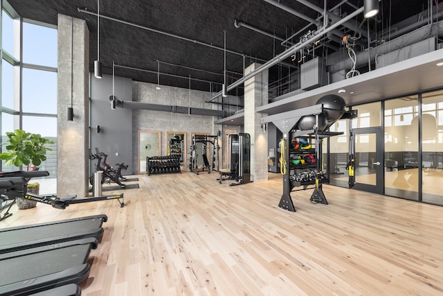 gym featuring hardwood / wood-style floors, a towering ceiling, and a healthy amount of sunlight