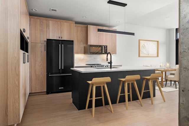 kitchen featuring pendant lighting, sink, a kitchen breakfast bar, black appliances, and an island with sink