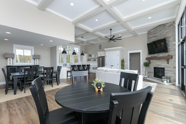 dining area featuring beamed ceiling, a stone fireplace, and light hardwood / wood-style flooring