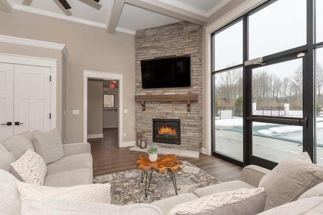 living room featuring beamed ceiling, wood-type flooring, a stone fireplace, and crown molding