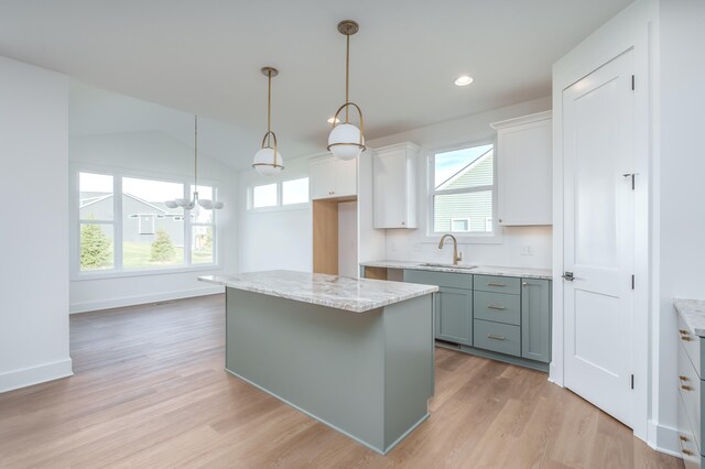 kitchen featuring sink, white cabinets, a kitchen island, decorative light fixtures, and light wood-type flooring