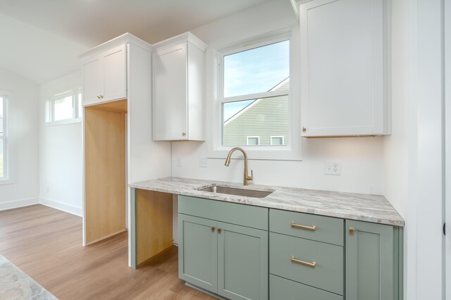 kitchen with white cabinetry, light stone countertops, sink, and light hardwood / wood-style floors