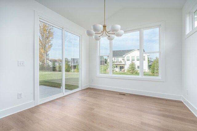 unfurnished dining area with plenty of natural light, a chandelier, vaulted ceiling, and light hardwood / wood-style flooring