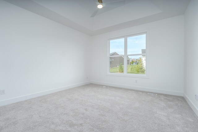 empty room with ceiling fan, a raised ceiling, and carpet