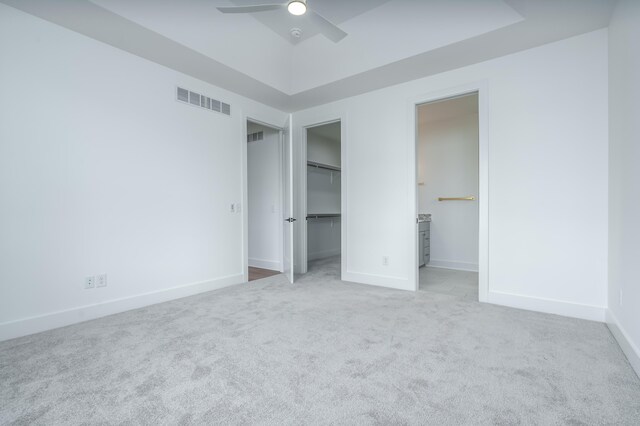 unfurnished bedroom featuring light carpet, a walk in closet, a closet, and ceiling fan