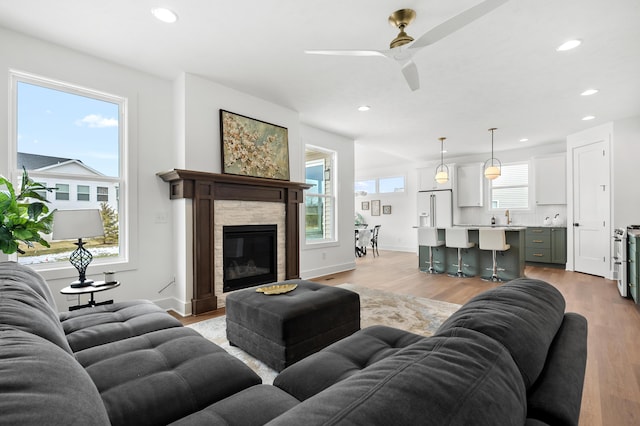 living room with ceiling fan, a stone fireplace, light hardwood / wood-style floors, and a wealth of natural light