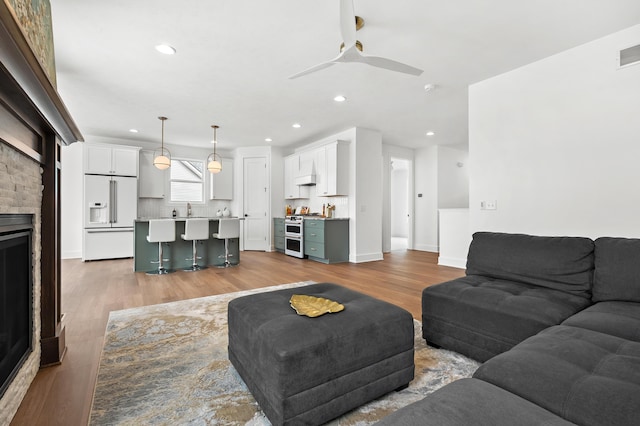 living room with ceiling fan, sink, a fireplace, and hardwood / wood-style floors