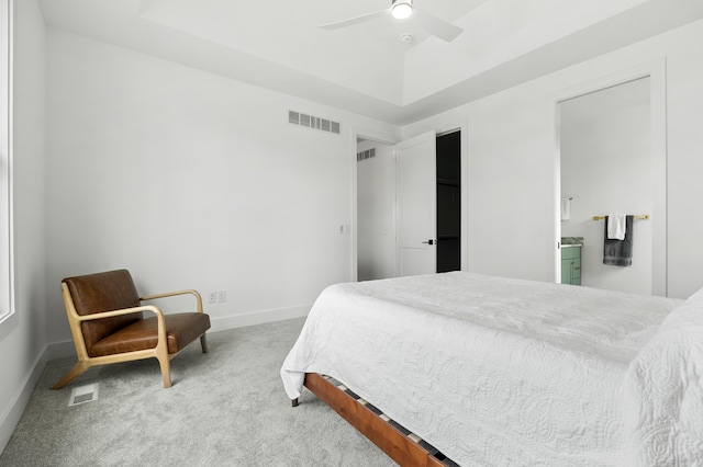 bedroom featuring a raised ceiling, ensuite bathroom, carpet floors, and ceiling fan