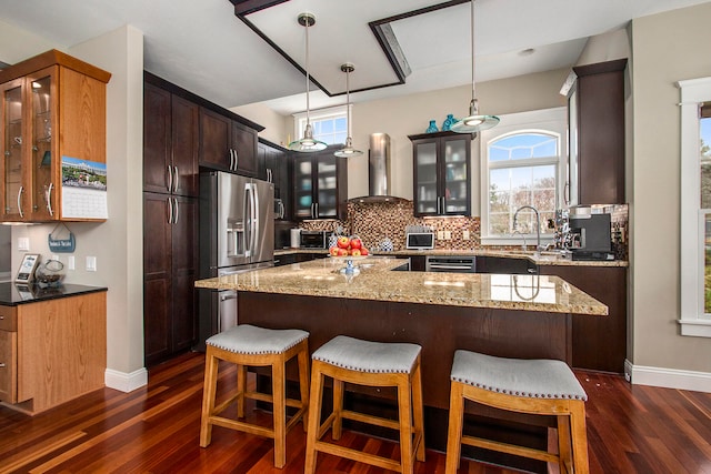 3975 Harbor Breeze Dr, Norton Shores, MI 49441 - kitchen with wall chimney range hood, stainless steel refrigerator with ice dispenser, dark wood finished floors, light stone countertops, and a center island