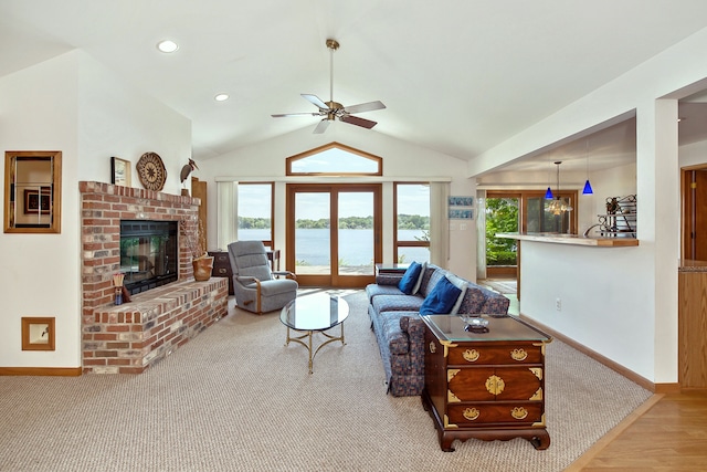 living room with ceiling fan, a water view, light hardwood / wood-style flooring, a fireplace, and lofted ceiling