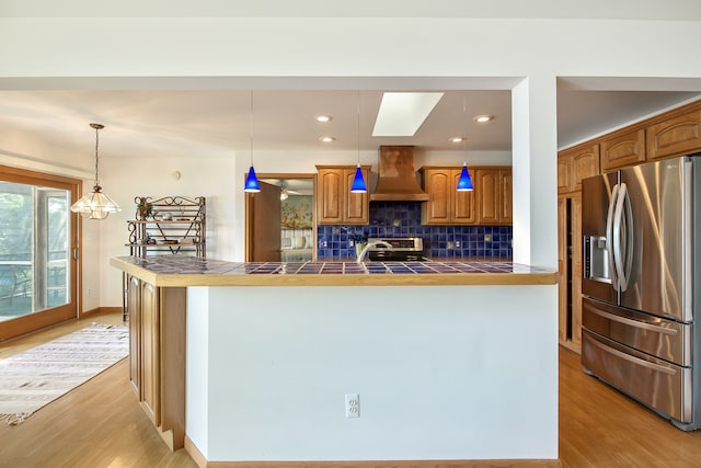 kitchen with tile countertops, wall chimney exhaust hood, hanging light fixtures, and appliances with stainless steel finishes