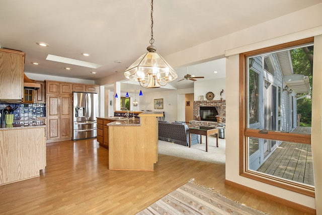 kitchen featuring stainless steel refrigerator with ice dispenser, ceiling fan with notable chandelier, light hardwood / wood-style flooring, a kitchen island, and hanging light fixtures