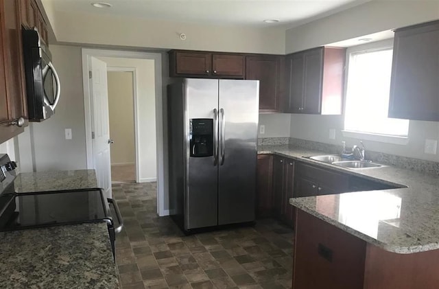 kitchen featuring dark brown cabinetry, sink, light stone counters, kitchen peninsula, and appliances with stainless steel finishes