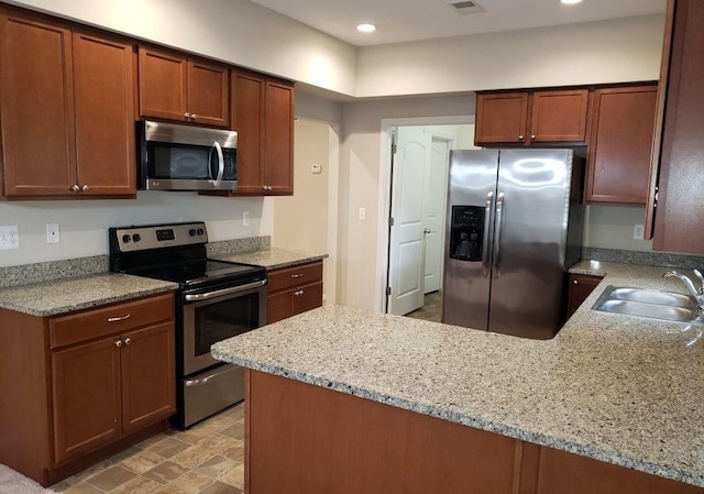 kitchen featuring kitchen peninsula, light stone counters, sink, and stainless steel appliances