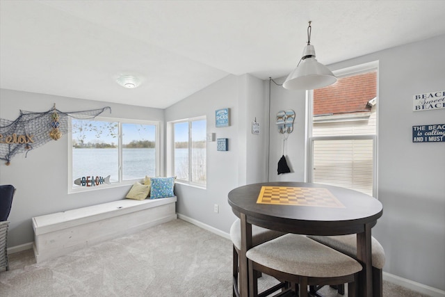 dining area featuring a water view, light colored carpet, and vaulted ceiling