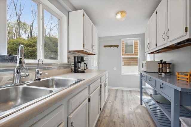 kitchen featuring decorative backsplash, white cabinetry, sink, and light hardwood / wood-style flooring