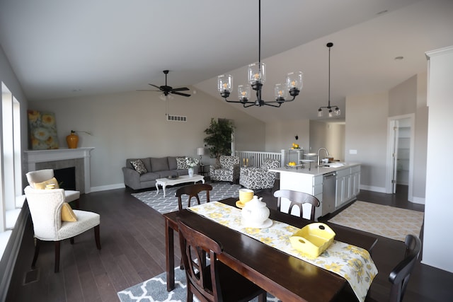 dining space featuring lofted ceiling, a tile fireplace, ceiling fan with notable chandelier, sink, and dark hardwood / wood-style floors