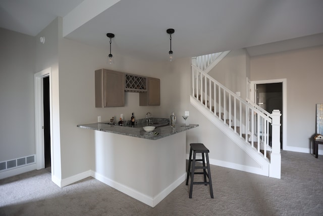 kitchen featuring light carpet, decorative light fixtures, kitchen peninsula, and light stone countertops