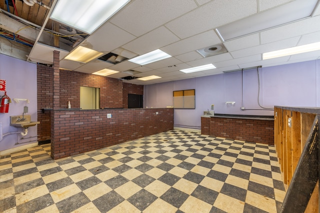 basement featuring a drop ceiling and brick wall