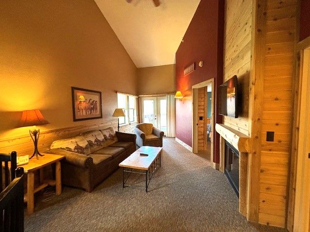 living room with carpet, french doors, high vaulted ceiling, and wood walls