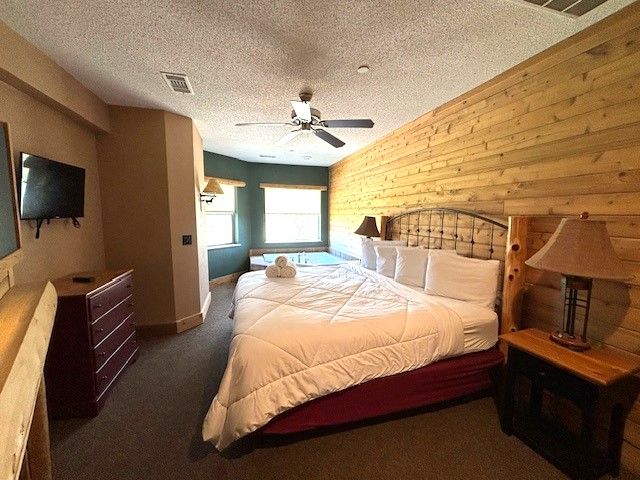 carpeted bedroom with ceiling fan, a textured ceiling, and wooden walls