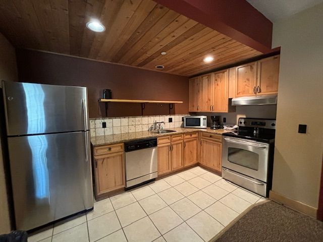 kitchen featuring backsplash, light tile patterned floors, stainless steel appliances, and wooden ceiling