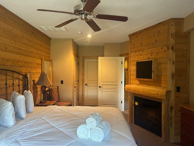 bedroom featuring ceiling fan, a large fireplace, a textured ceiling, and wooden walls