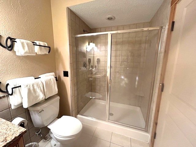 bathroom featuring tile patterned flooring, a shower with shower door, a textured ceiling, and toilet