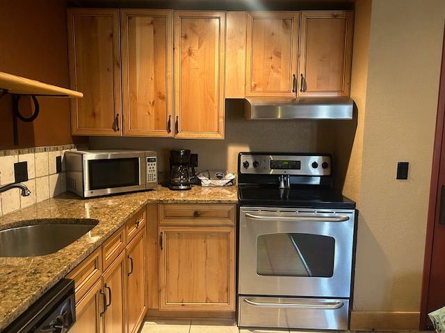 kitchen featuring appliances with stainless steel finishes, tasteful backsplash, light stone counters, sink, and light tile patterned floors