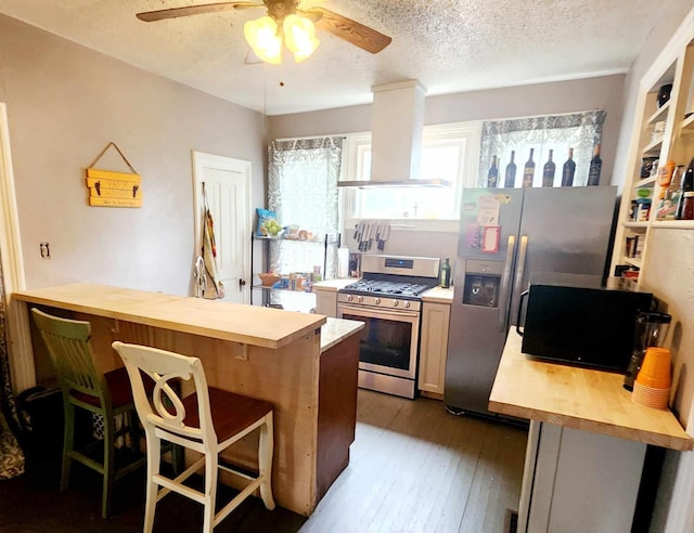 kitchen with a kitchen bar, appliances with stainless steel finishes, a textured ceiling, ventilation hood, and hardwood / wood-style flooring