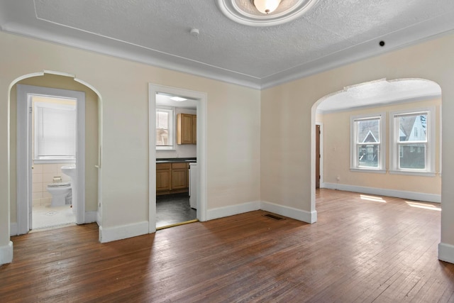 empty room featuring crown molding, a healthy amount of sunlight, dark hardwood / wood-style flooring, and a textured ceiling