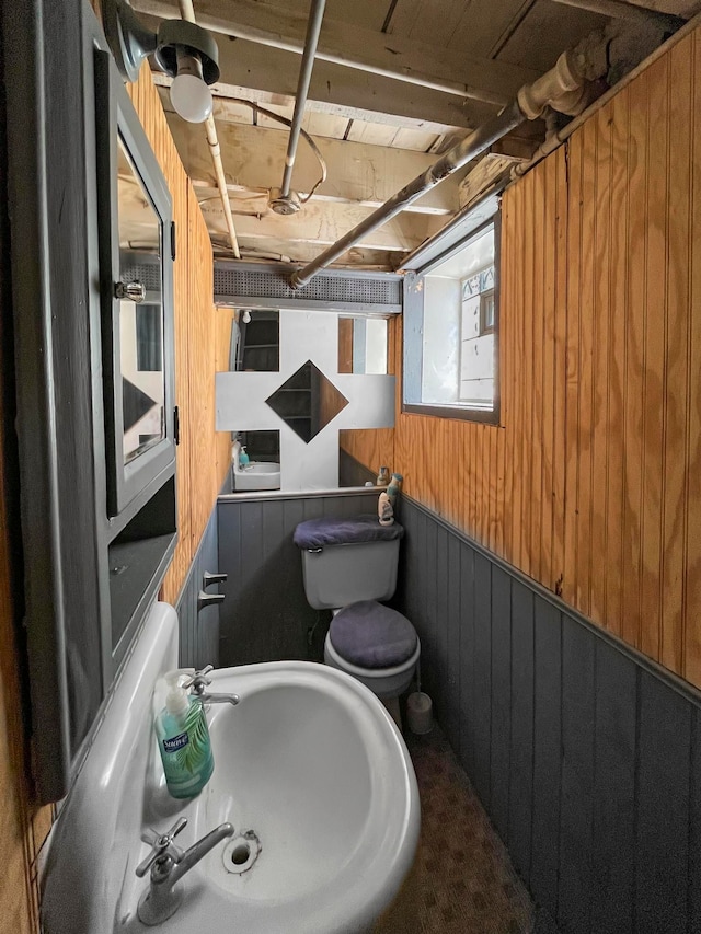 bathroom with sink, toilet, and wood walls