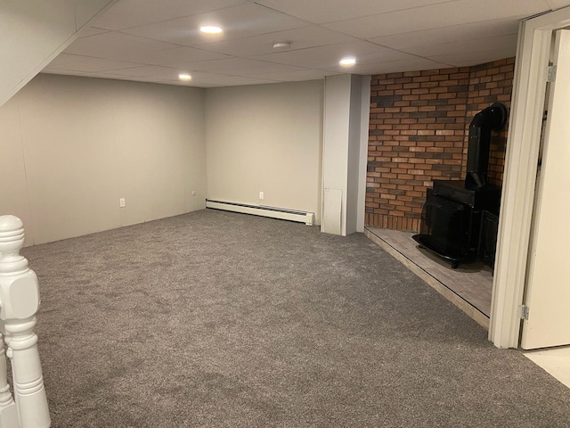 basement with carpet floors, a baseboard radiator, a wood stove, and a drop ceiling