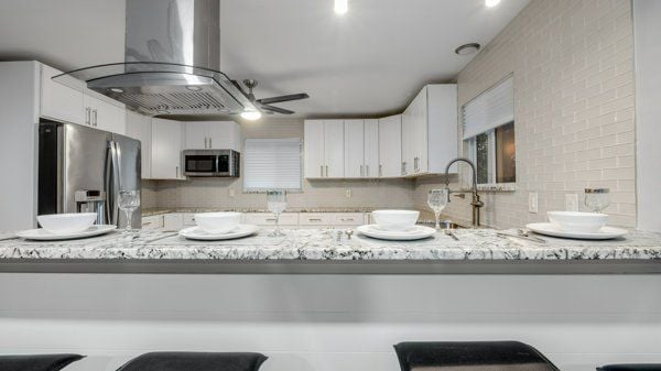 kitchen featuring kitchen peninsula, white cabinetry, island exhaust hood, and appliances with stainless steel finishes