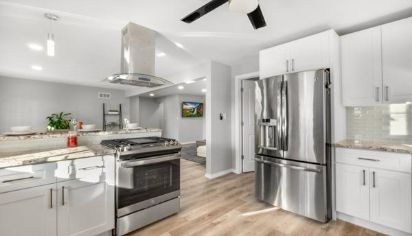 kitchen with white cabinets, wall chimney exhaust hood, ceiling fan, and stainless steel appliances