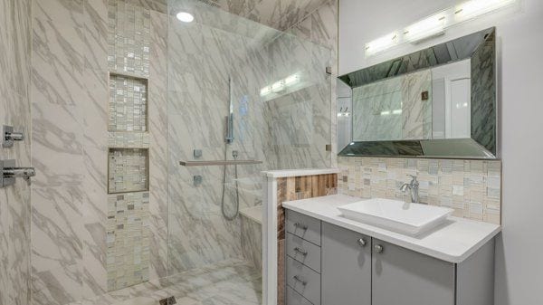 bathroom featuring tiled shower, vanity, and tile walls