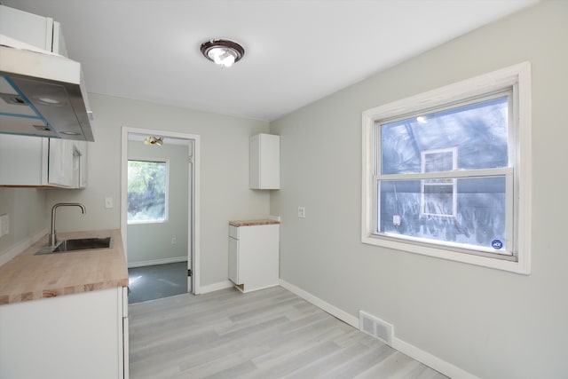 kitchen with white cabinets, light hardwood / wood-style floors, sink, and exhaust hood