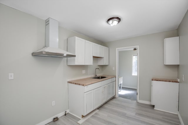 kitchen featuring wood counters, white cabinets, wall chimney range hood, sink, and light wood-type flooring