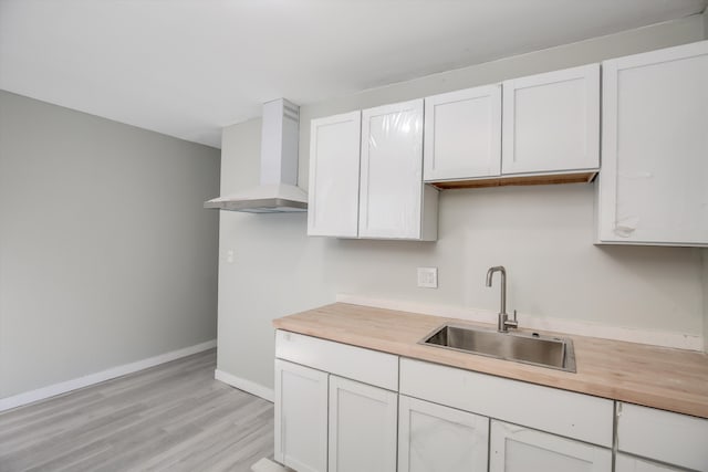 kitchen with white cabinets, light wood-type flooring, wall chimney exhaust hood, and sink