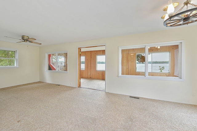 carpeted empty room featuring a wealth of natural light, a water view, and ceiling fan with notable chandelier