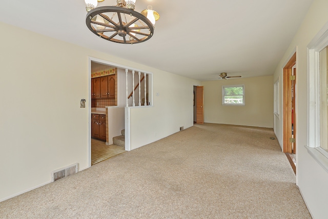 empty room with ceiling fan with notable chandelier and light colored carpet