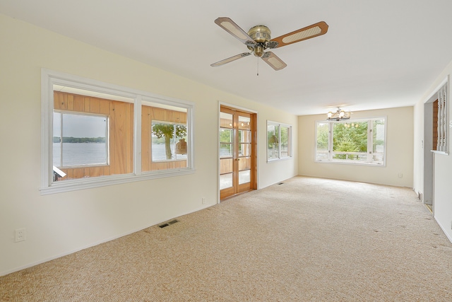 unfurnished room with a wealth of natural light, carpet, and ceiling fan with notable chandelier