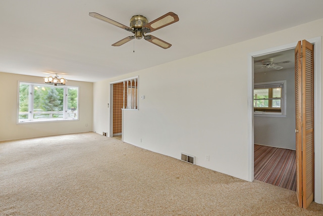 unfurnished room with ceiling fan with notable chandelier and light carpet