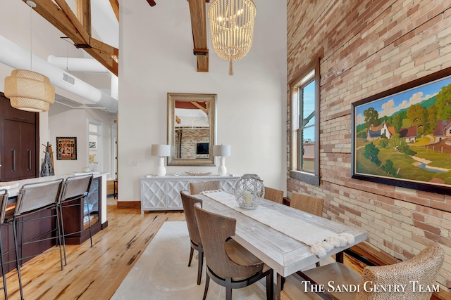 dining room with light hardwood / wood-style floors, a towering ceiling, brick wall, and a chandelier