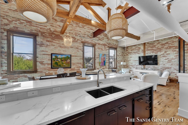 kitchen with high vaulted ceiling, sink, light hardwood / wood-style flooring, dark brown cabinetry, and brick wall