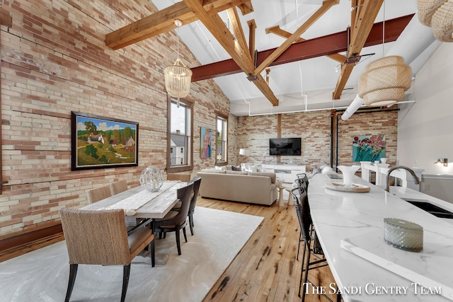 dining area with brick wall, sink, beam ceiling, high vaulted ceiling, and light hardwood / wood-style flooring