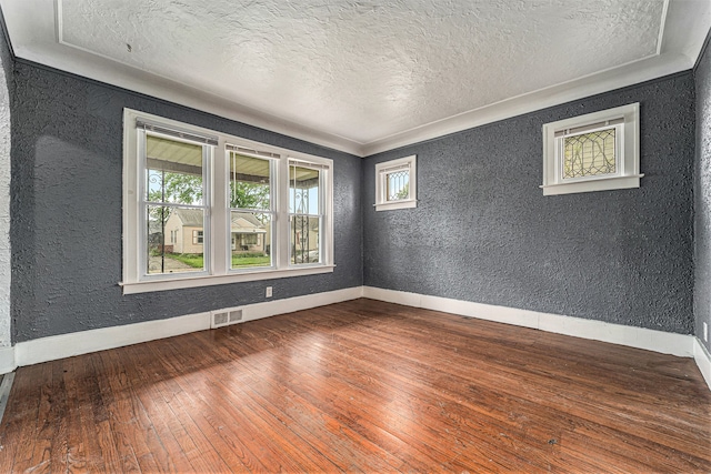 empty room featuring hardwood / wood-style floors, a textured ceiling, and ornamental molding